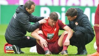 FCK-Spieler Kevin Kraus sitzt verletzt auf dem Spielfeld und wird behandelt.