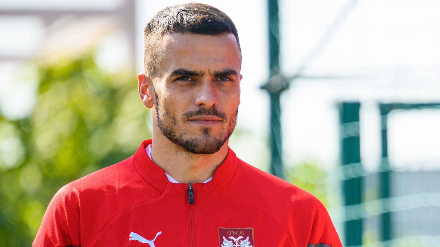 Filip Kostić trägt eine rote Sportjacke der serbischen Fußballnationlmannschaft und schaut nach vorne.