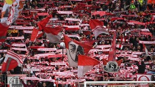 Fans des SC Freiburg im Europa-League-Stadion schwenken Fahnen und Schals.