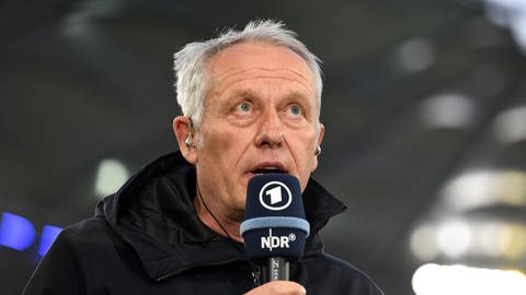 Christian Streich hält ein Fernsehmikrofon und gibt ein Interview