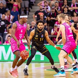 Silas Melson (schwarzes Trikot) von den MHP Riesen Ludwigsburg verteidigt gegen Glynn Watson und Till Pape von den Telekom Baskets Bonn