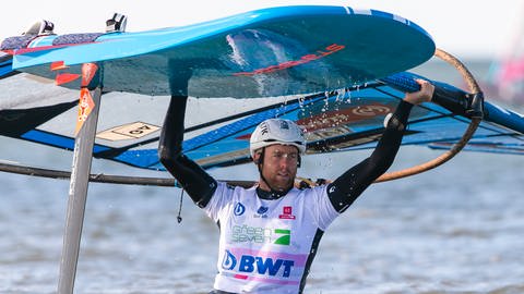 Windsurfer Sebastian Kördel aus Radolfzell trägt nach einem Rennen in der Disziplin Foil sein Material aus dem Wasser.