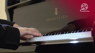 Standbild aus dem Dokumentarfilm Wir fangen ganz von vorne an: Hände von Pianist Igor Levit spielen auf einem Flügel, rotes Overlay mit Icon Filmrolle