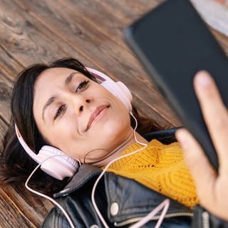 SWR1 zum Hören, wann und wo Sie wollen (Foto: Frau mit Kopfhörern und Smartphone liegt auf dem Holzboden)