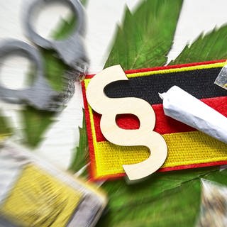 Symbolbild: Joint, Paragrafenzeichen und Deutschland-Fahne auf Cannabis-Blatt mit Handschellen