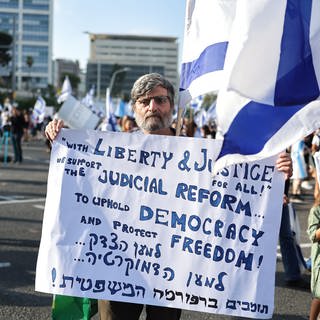 Ein Mann hält ein Plakat bei einer Demonstration zur Unterstützung der Pläne der Regierung um Ministerpräsident Netanjahu zur Überarbeitung des Justizsystems. Während in Tel Aviv tausende Unterstützer des geplanten Justizumbaus zusammenkamen, versammelten sich in Jerusalem Tausende, die dem Vorhaben ablehnend gegenüberstehen.