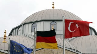 Eine europäische, eine deutsche und eine türkische Fahne (l-r) wehen am Freitag (10.09.2010) vor der Merkez-Moschee in Duisburg vor dem Beginn des Freitagsgebets. Die Debatte um die geplante Koran-Verbrennung in Florida hat die Feiertagsruhe der Muslime zum Ende des Ramadans gestört