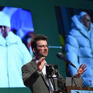 Der Netzjournalist Gregor Schmalzried spricht bei der Eröffnung des 7. Evangelischen Medienkongresses im Sendesaal des Hessischen Rundfunks (hr) vor einer Projektion mit KI-generierten Fotos von Papst Franziskus. Der zweitägige Kongress zum Thema Künstliche Intelligenz steht unter dem Motto «Im Anfang war das Wort - am Ende der Chat?