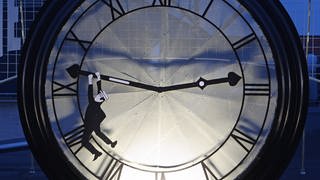 Mann hängt am Zeiger einer großen Uhr
