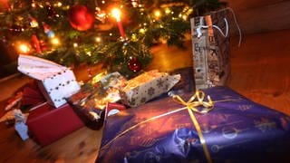 Verpackte Geschenke liegen in einem Wohnzimmer unter einem festlich geschmücktem Weihnachtsbaum.
