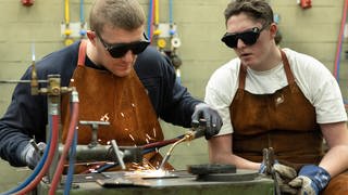 Ein Auszubildender  Lehrling im Beruf Metallbauer wird von seinem Meister im Schweissen unterrichtet