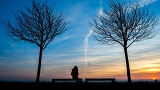 Achtsamkeit, Reslilienz. Mit Krisen umgehen, Frau Sitz auf Bank im Sonnenuntergang