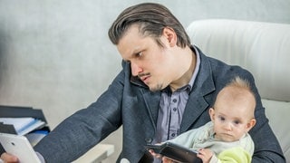 Ein junger Geschäftsmann arbeitet in seinem Büro und hält ein Baby