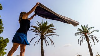 Eine Frau breitet am Strand ihr Handtuch aus. Endlich wieder Urlaub mit Strand und Pool.