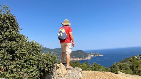 Ein Tourist geht bei wolkenlosen Himmel auf der griechischen Insel Skopelos wandern.