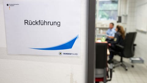 Beamte arbeiten in der Bundespolizeiinspektion Ludwigsdorf in einem Büro mit dem Schild „Rückführung“. Ministerpräsident Kretschmer informierte sich bei einem Besuch über die Situation an der deutsch-polnischen Dienststelle.