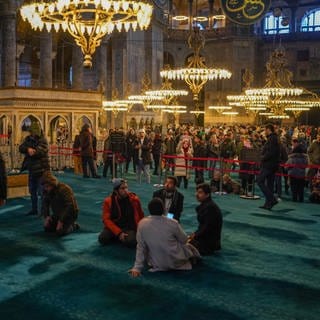 Muslime beten im linken Bereich der Hagia Sophia, während Touristen das Museum auf der rechten Seite besuchen.