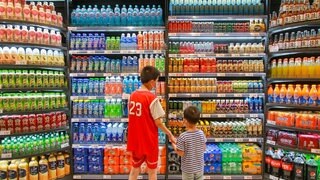 Zwei Jungs stehen in einem Supermarkt vor einem Kühlregal und suchen sich Getränke aus. 