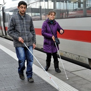 Zwei blinde Menschen gehen am Hauptbahnhof in München (Bayern) an einem ICE vorbei.