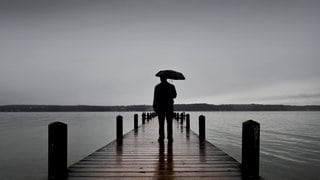 Ein Mensch mit Regenschirm steht auf einer Brücke