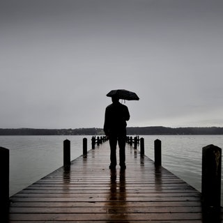 Ein Mensch mit Regenschirm steht auf einer Brücke