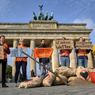 Mitglieder der "Letzten Generation" stehen mit Plakaten und Sandsäcken vor dem Brandenburger Tor und protestieren gegen den Klimawandel.