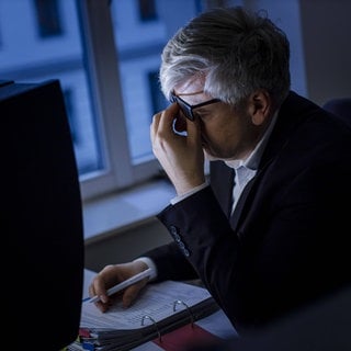 Ein Mann sitzt spaet abends erschoepft an einem Schreibtisch.