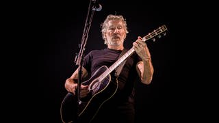 Pink Floyd Sänger Roger Waters steht auf einer Bühne und spielt Gitarre.