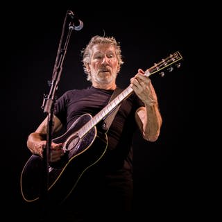 Pink Floyd Sänger Roger Waters steht auf einer Bühne und spielt Gitarre.