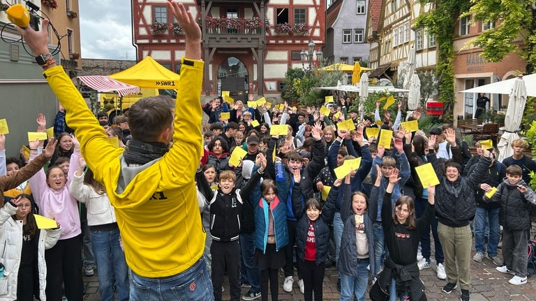 HITmach-Duell Besigheim: Corvin Tondera-Klein steht mit hochgerissenen Armen vor einem großen Schulchor der Maximilian-Lutz-Realschule.