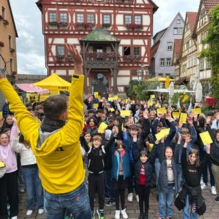 HITmach-Duell Besigheim: Corvin Tondera-Klein steht mit hochgerissenen Armen vor einem großen Schulchor der Maximilian-Lutz-Realschule.