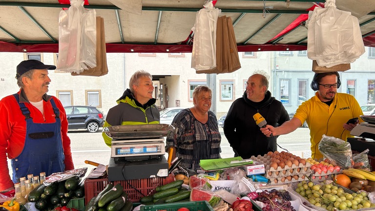 HITmach-Duell Nußloch: Ingo Lege am Markstand vor Obst und Gemüse singt mit den Marktstand-Betreibern.