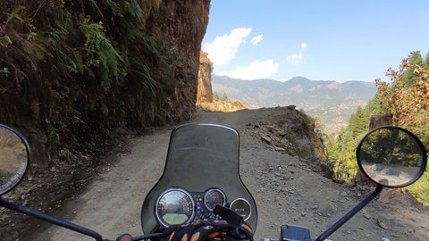 Blick über den Lenker auf die staubige Straße von SWR1 Hörer Wolfgang in Indien mit Bergen im Hintergrund.