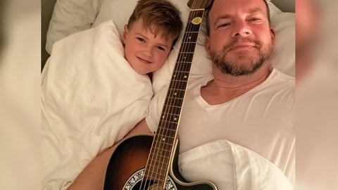 SWR1 Hörer Martin liegt mit seinem Sohn und einer Gitarre im Bett.