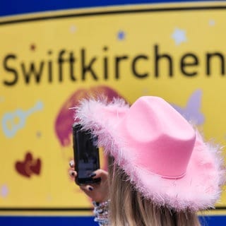 Ein Fan fotografiert in der Gelsenkirchener Innenstadt ein Schild mit der Aufschrift "Swiftkirchen". Die Konzerte von Taylor Swift in Deutschland haben Einfluss auf die SWR1 Hitparade.