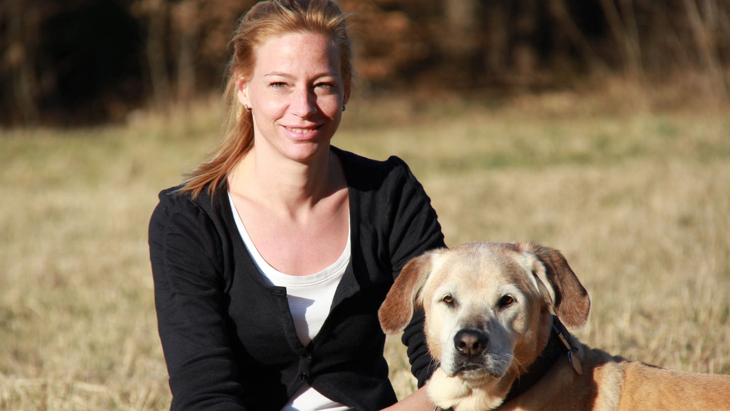 Julia Fritz sitzt mit ihrem Hund im Grünen.