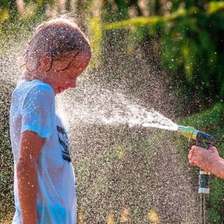 Abkühlung im Sommer: ein Mädchen bespritzt einen Jungen mit Wasser aus dem Gartenschlauch, beide lachen und freuen sich