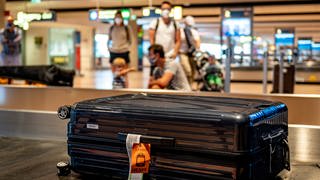 Eine Familie wartet am Gepäckband eines Flughafens auf ihren Koffer.