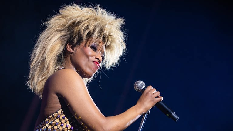 Aisata Blackman spielt Tina Turner im Musical TINA in Stuttgart. Sie steht auf der Bühne mit einem Mikrofon in der Hand.