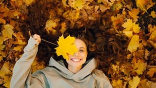 Eine Frau liegt lachend im Herbstlaub.