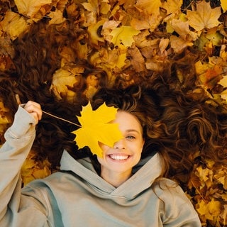 Eine Frau liegt lachend im Herbstlaub.