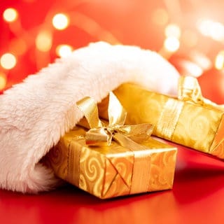 Wundervolles Winterwissen - der SWR1 Adventskalender: Warum packen wir Geschenke ein? Das Bild zeigt Geschenke, die in goldenes Geschenkpapier gewickelt und mit goldenen Schleifen versehen sind. Sie stecken halb in eine roten Nikloaus-Mütze mit weißem Fellbesatz.