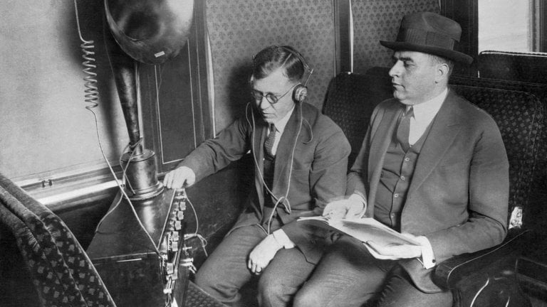 Wissen was 2023 war und bares Geld beim Quiz "SWR1 Tasse oder Kasse" gewinnen. (Foto Schwarz-weiß: Zwei Männer hören in den 1920er Radio)