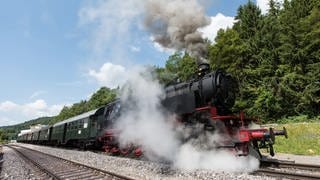 Die Dampflokomotive der Sauschwänzlebahn mit angehängten Personenzugwagen am Bahnhof Weizen bei Blumberg. Dampf umhüllt die Räder der Lok.