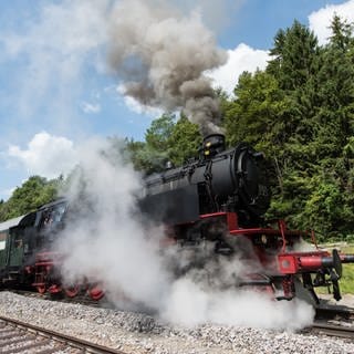 Die Dampflokomotive der Sauschwänzlebahn mit angehängten Personenzugwagen am Bahnhof Weizen bei Blumberg. Dampf umhüllt die Räder der Lok.