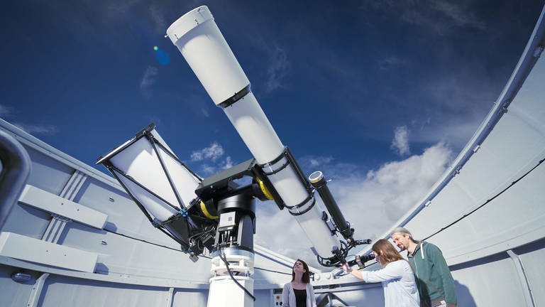 Eine Frau in einer Sternwarte schaut durch ein großes, weißes Teleskop.