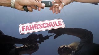 Ein Fahrlehrer überreicht seiner Fahrschülerin den Schlüssel zum Fahrzeug.