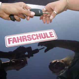 Ein Fahrlehrer überreicht seiner Fahrschülerin den Schlüssel zum Fahrzeug.