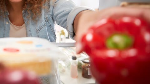 Eine Frau schaut in einen Kühlschrank, der mit frischem Gemüse gefüllt ist