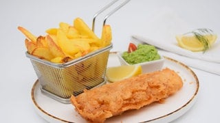 Auf einem Teller liegen Fish and Chips, also ein paniertes Fisch-Filet und ein Körbchen Pommes. In England kommt man nicht drumrum und zur Fußball-EM 2024 auch nicht bei uns. Fish and Chips. Von der Insel auf den Teller: Enjoy your meal! 